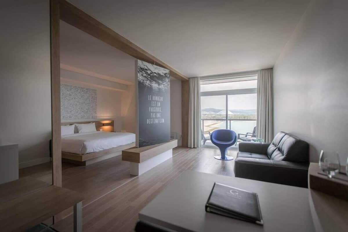 Een moderne hotelkamer met een bed, een zithoek, een groot raam en uitzicht op de omgeving.