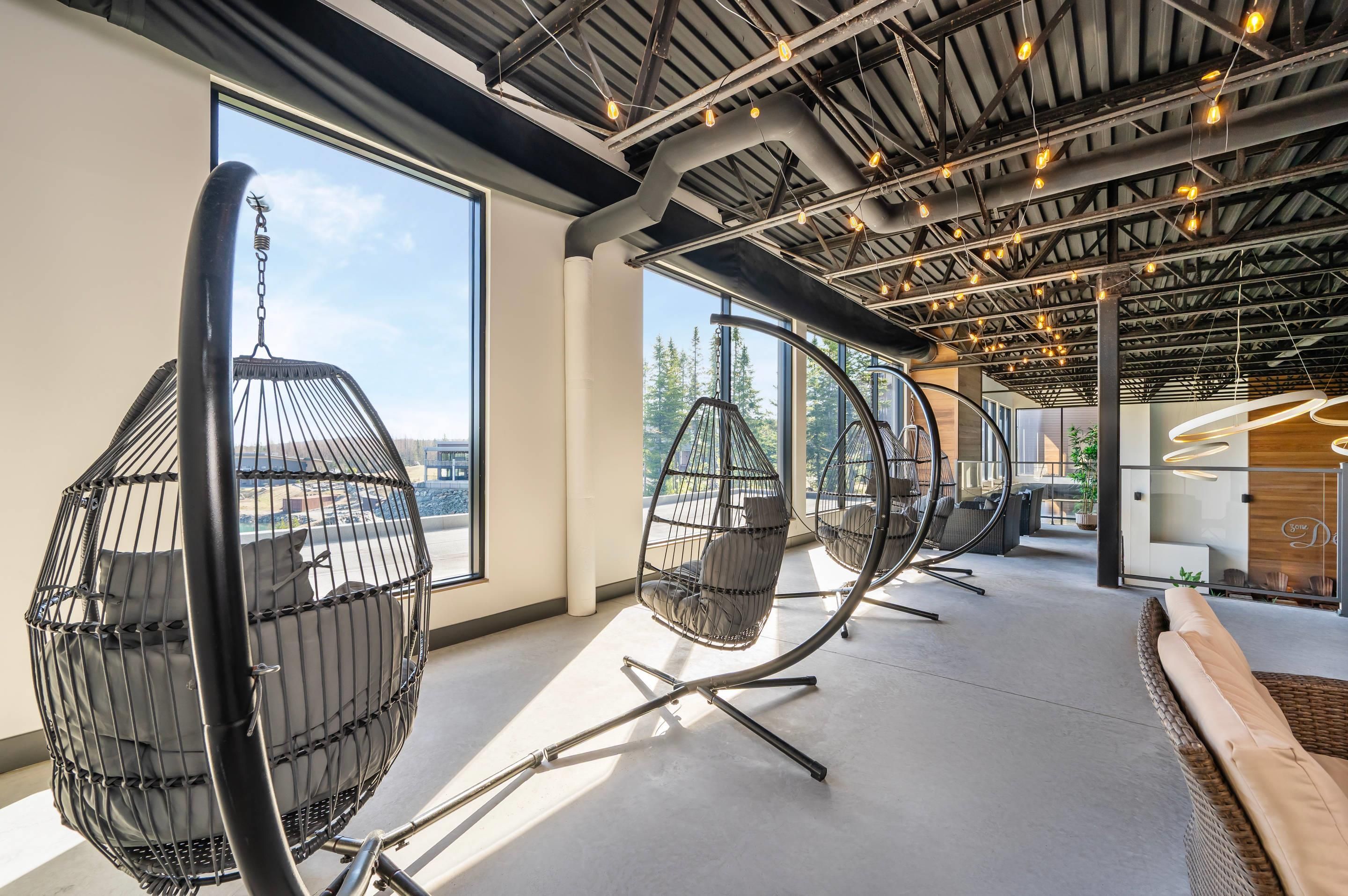 Een modern interieur met hangstoelen, grote ramen en een hoge plafond met zichtbare balken.