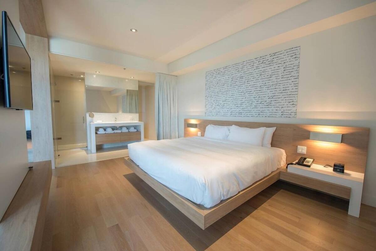 Een moderne slaapkamer met een groot bed, nachtkastjes, een spiegel en een kunstwerk aan de muur.
