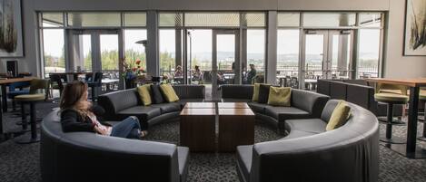 A modern lounge area with a curved seating arrangement, large windows offering a view of the city, and a central coffee table.