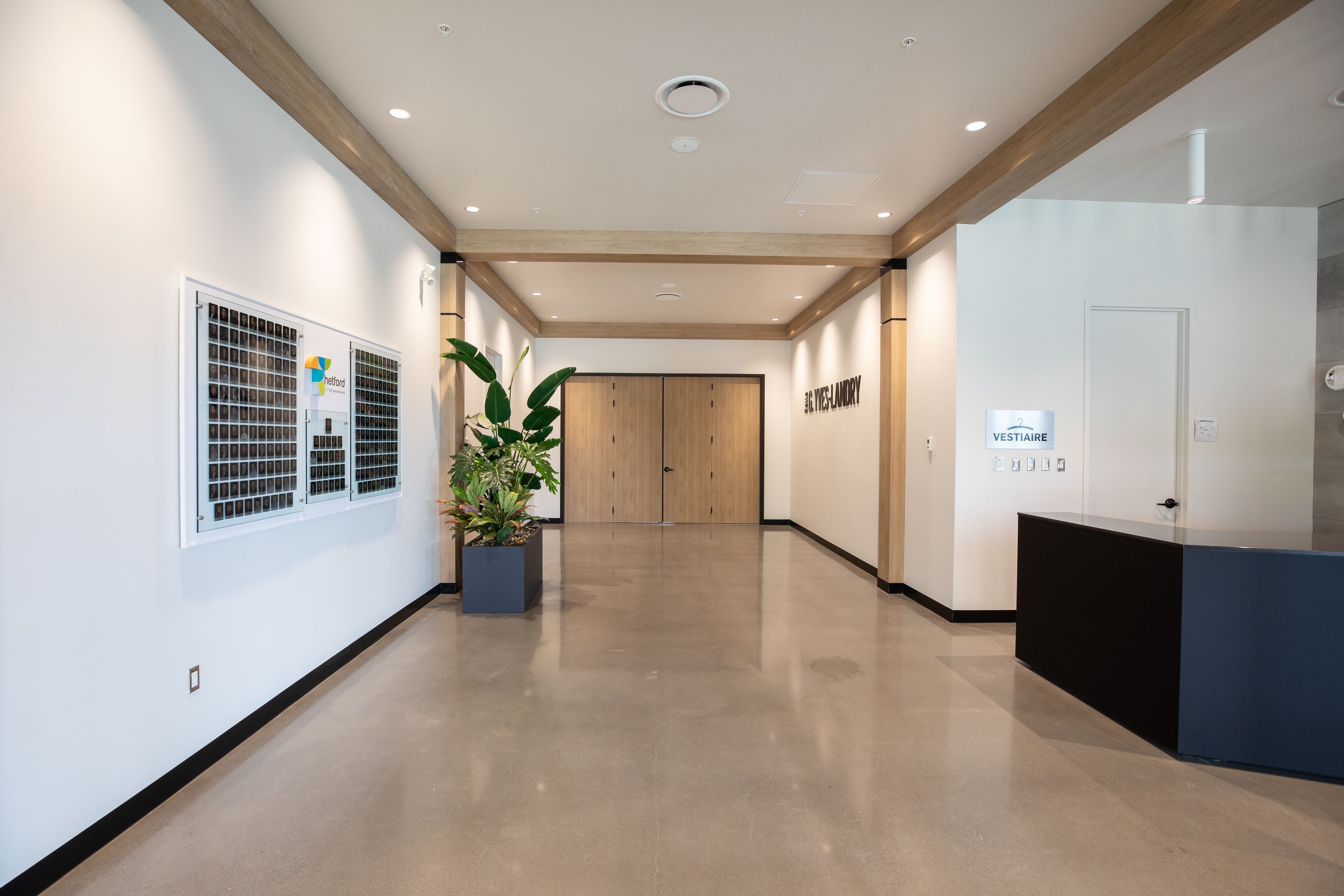 Un pasillo moderno con una recepción, una planta en maceta y una puerta que indica “VESTIAIRE”.