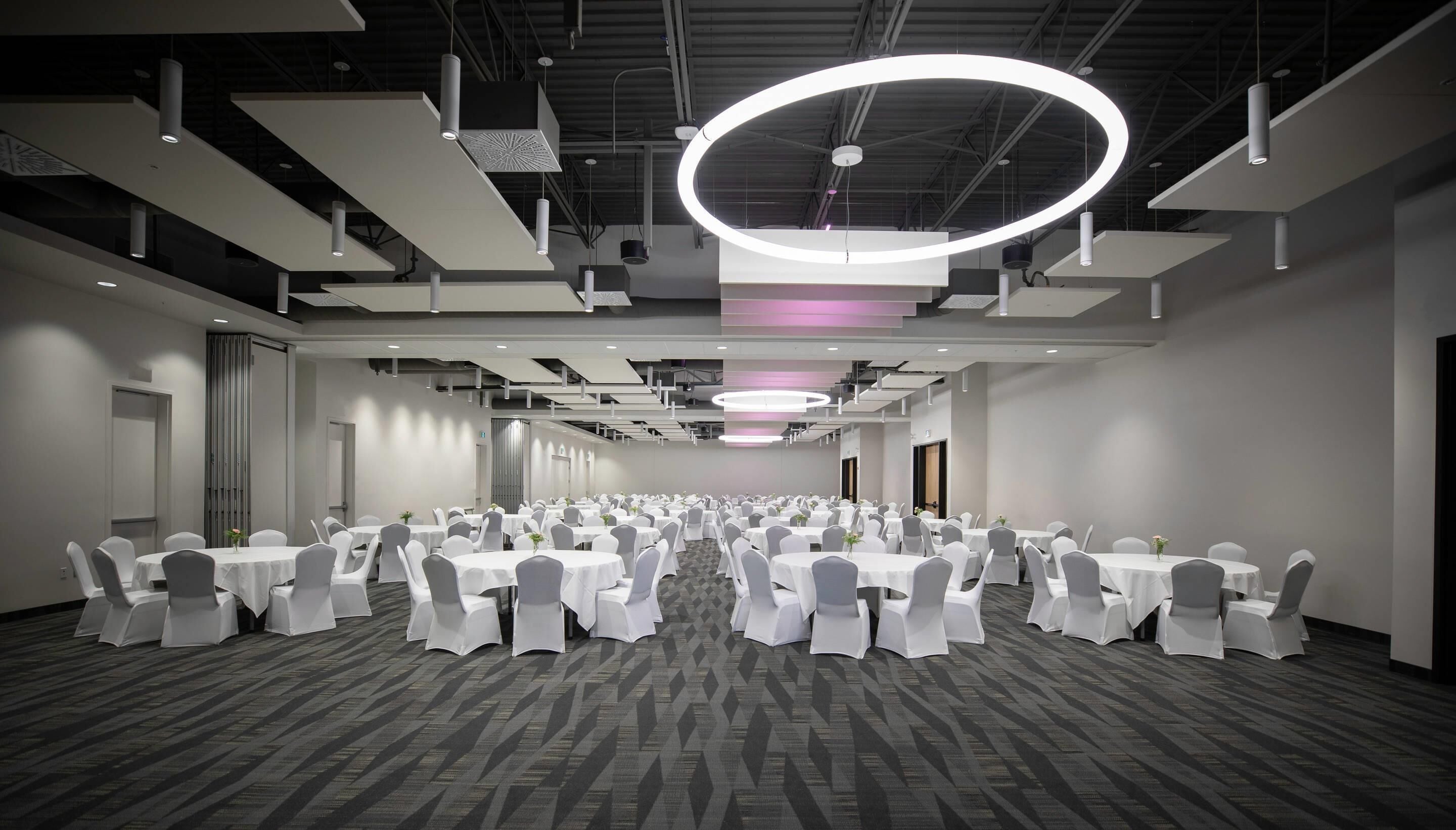 A large conference room with multiple round tables, white chairs, and a patterned carpet.
