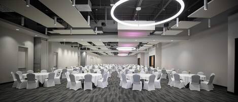 A large conference room with multiple round tables, white chairs, and a patterned carpet.