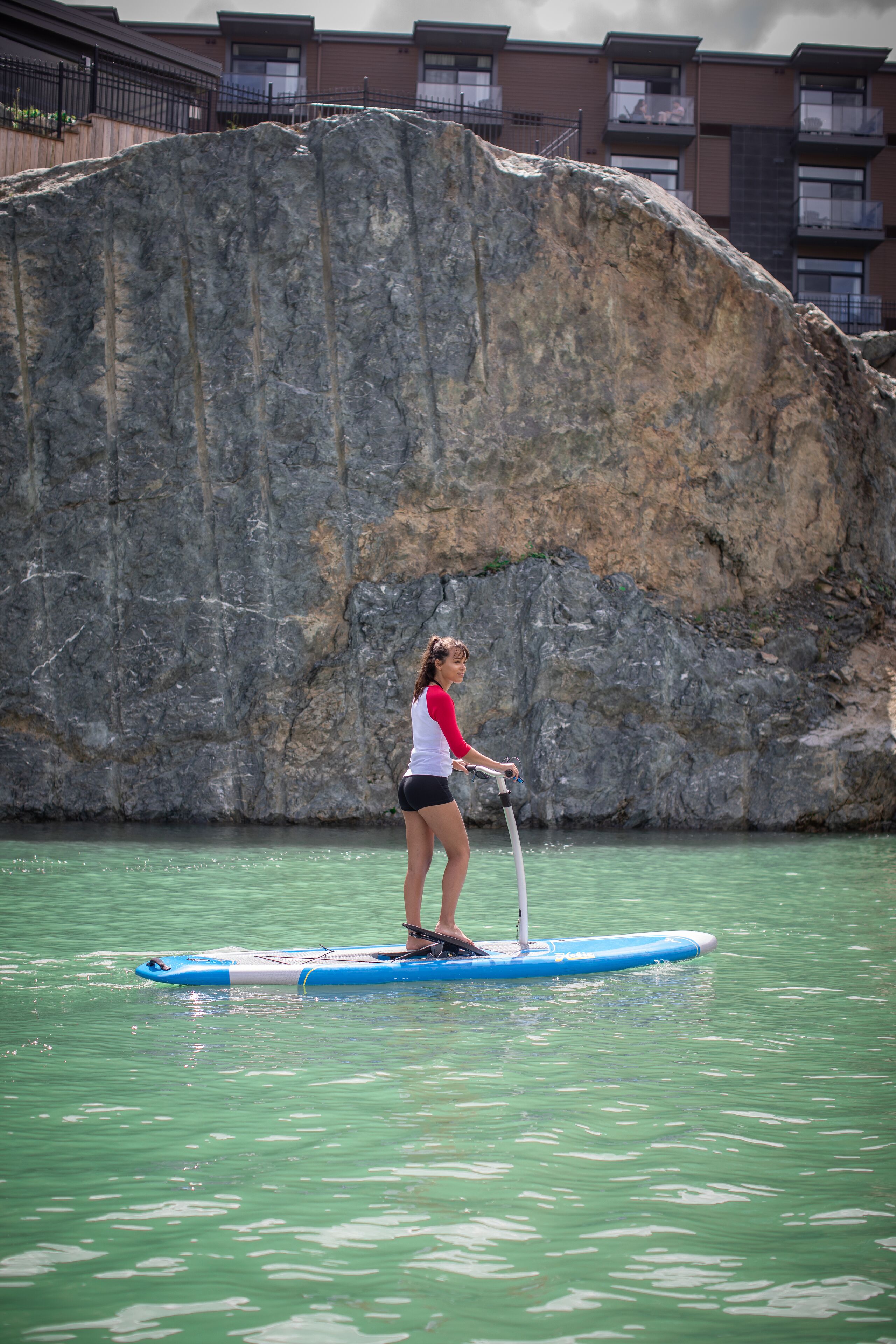 A person paddleboarding on a calm body of water with a rocky cliff in the background.