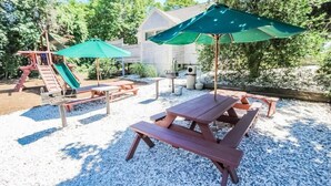 Une cour arrière avec des tables de pique-nique, un toboggan et une maison en arrière-plan.