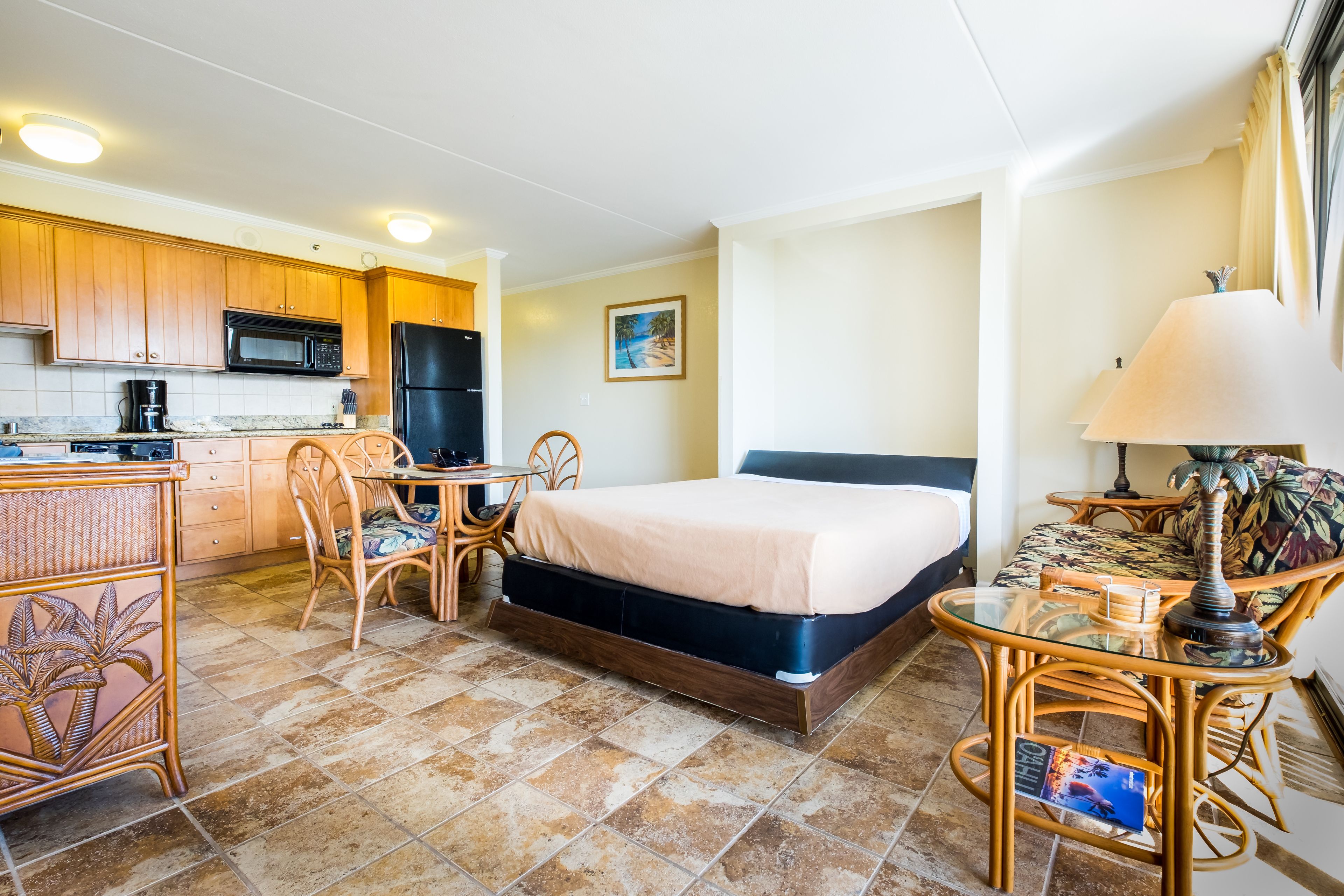 A compact hotel room with a kitchenette, a bed, a dining table, and a chair.