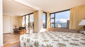 A hotel room with a large bed, a desk, a chair, and a view of the city through large windows.