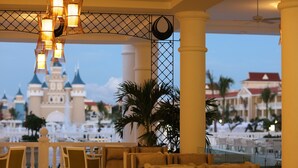 A hotel lobby with a view of a castle, seating areas, and a ceiling fan. - Bahia Principe Explore Legend - Hyatt Inclusive Collection - All Inclusive (Punta Cana)