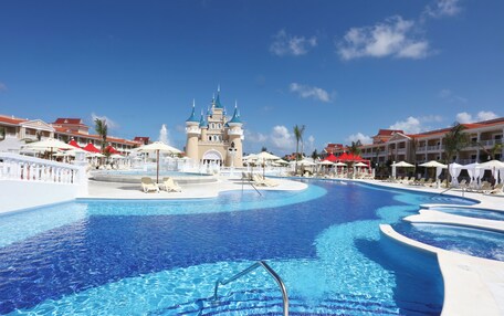 A large swimming pool with a castle-like structure in the center, surrounded by lounge chairs and umbrellas.