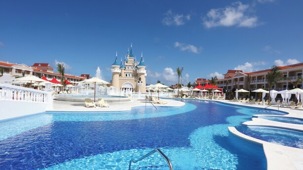 Una gran piscina con una estructura tipo castillo en el centro, rodeada de sillones y sombrillas.