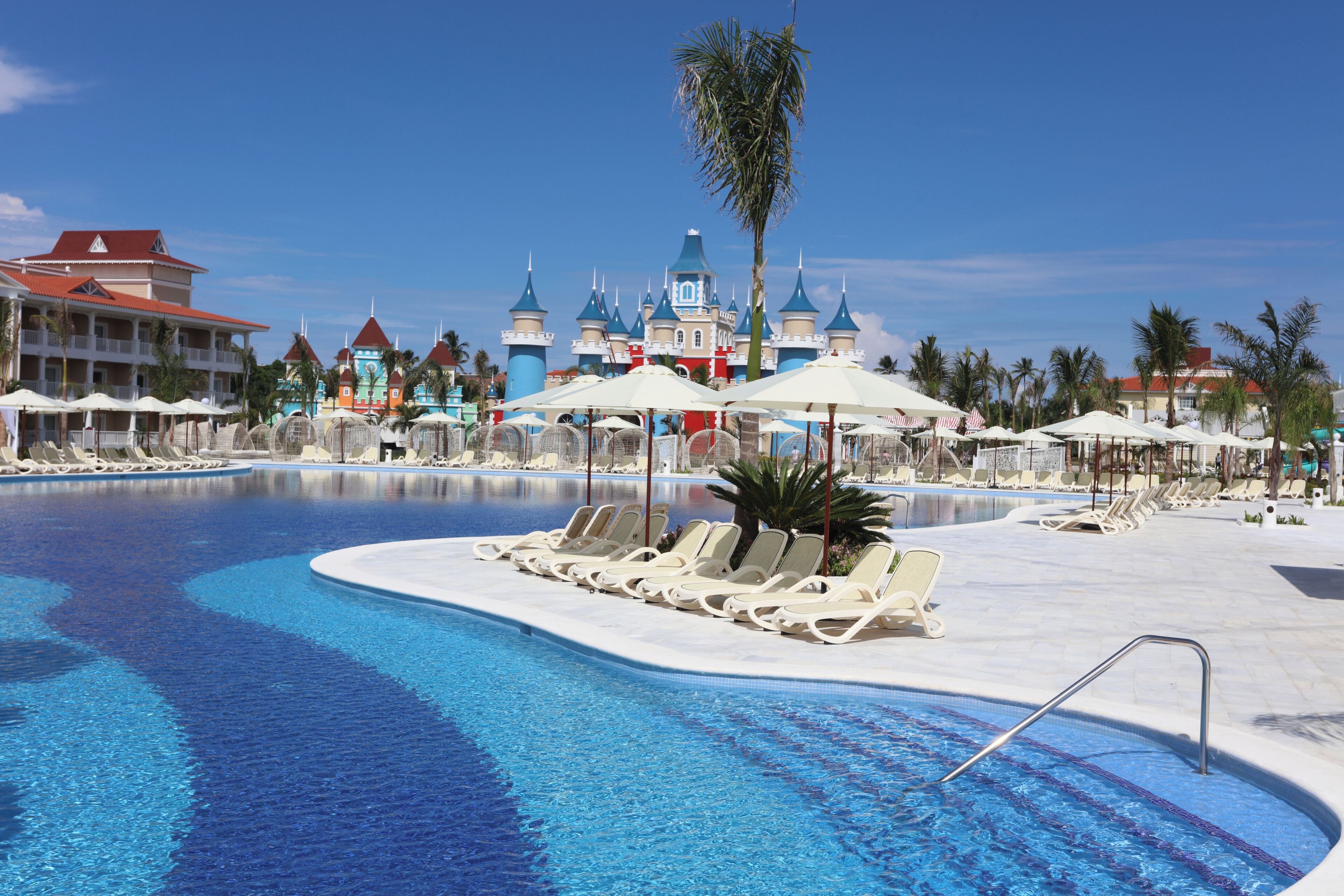 A swimming pool with lounge chairs, umbrellas, and a castle-like building in the background.