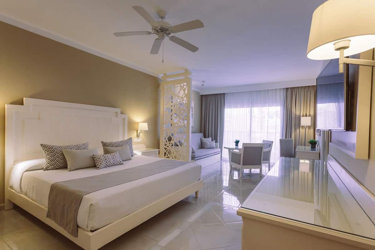 Une chambre d’hôtel équipée d’un lit, d’un bureau, d’une chaise, d’un ventilateur de plafond et d’un grand miroir.
