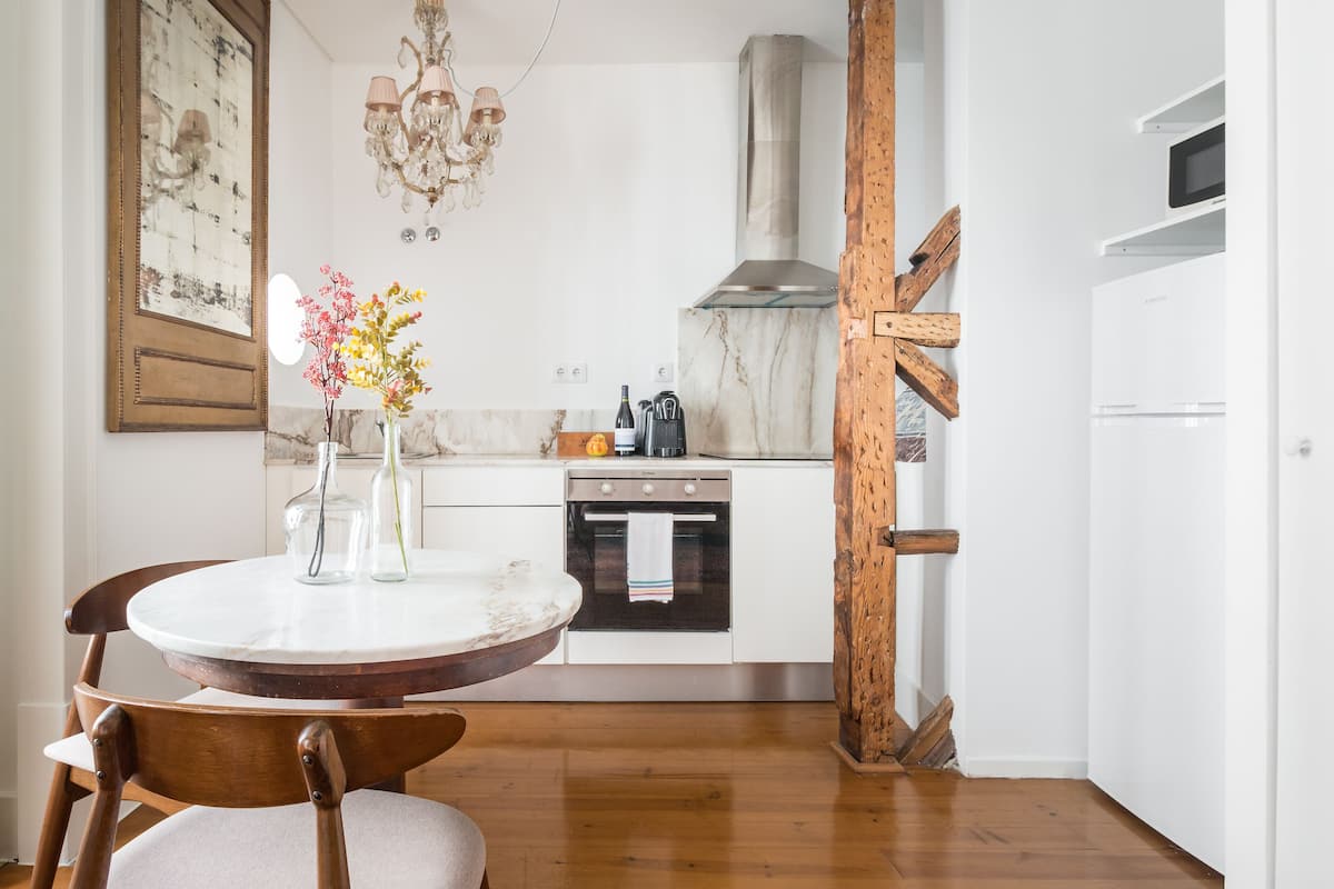 A kitchen with white cabinets, a marble countertop, a wooden chair, and a vase with flowers.