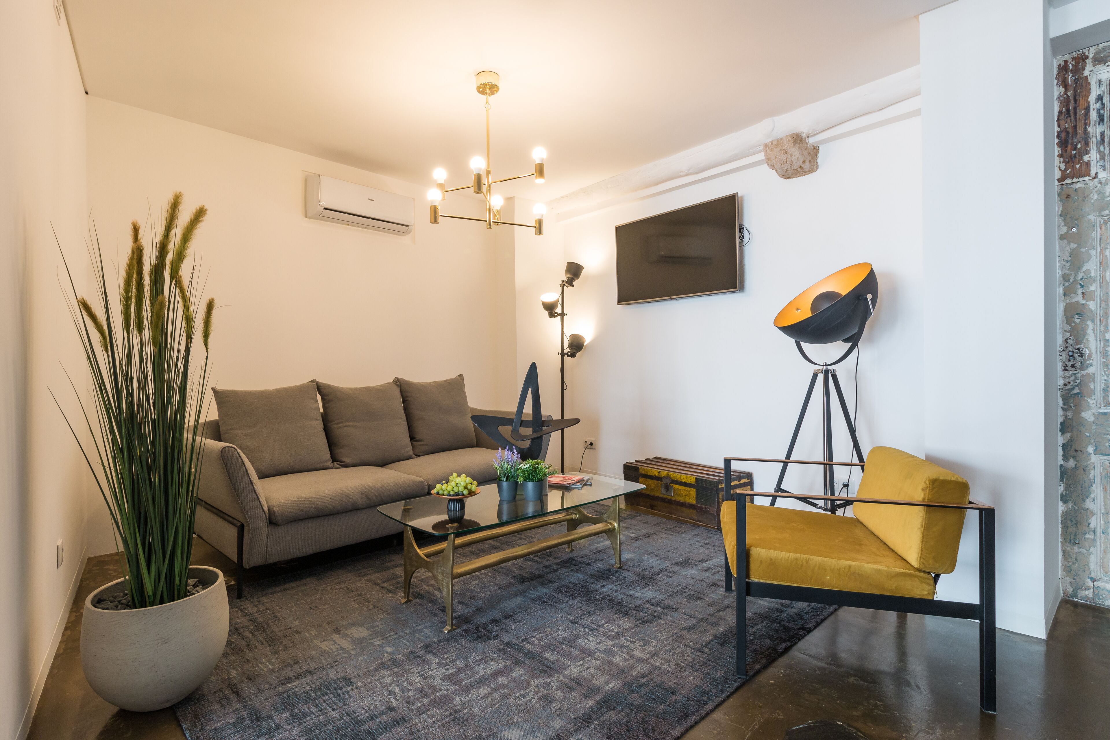 Una sala moderna con un sofá, una mesa de centro y un sillón amarillo. Hay una planta en maceta y una lámpara de pie.