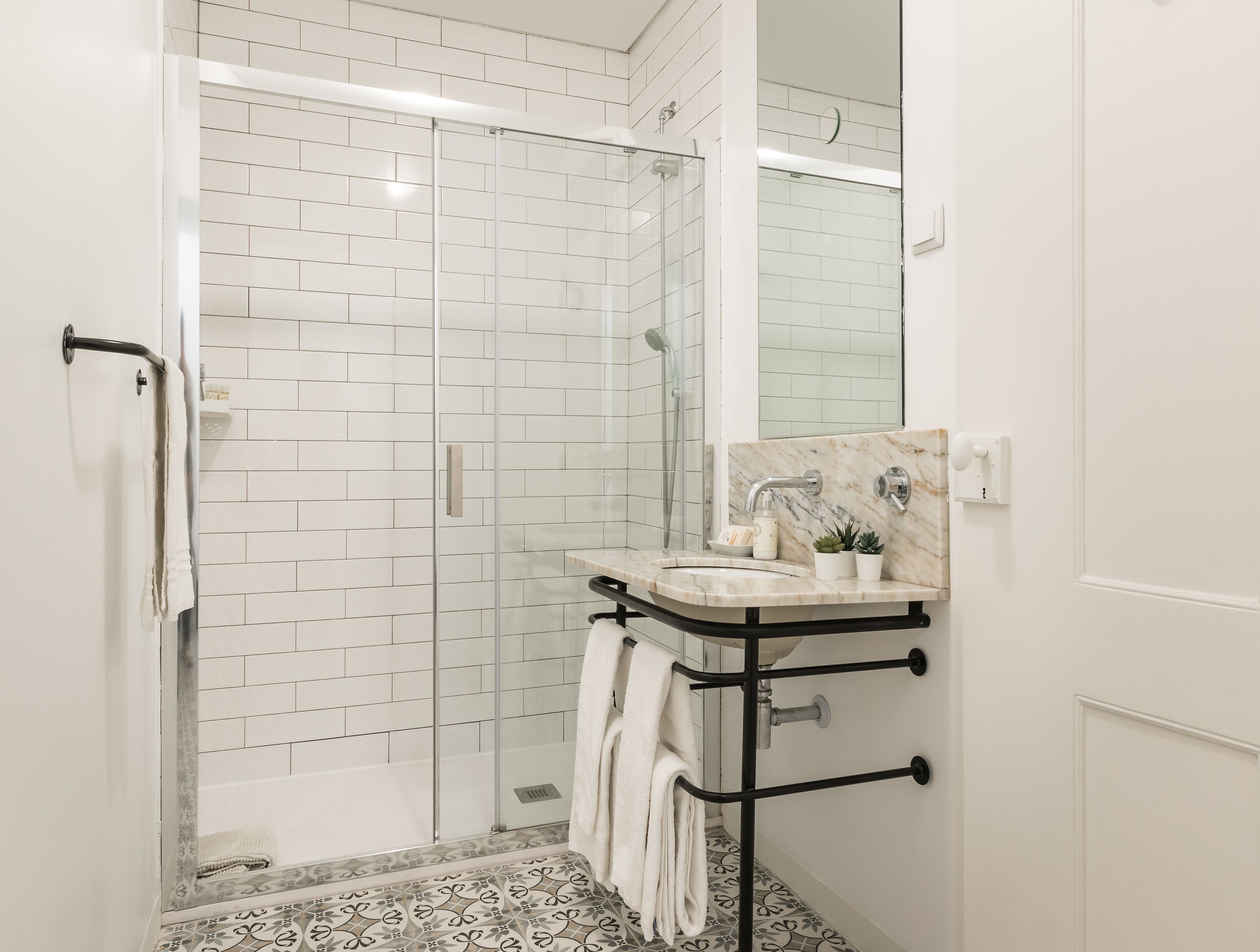 Un bagno moderno con doccia vetrata, pareti piastrellate di bianco, un piano di lavoro in marmo e un porta asciugamani nero.