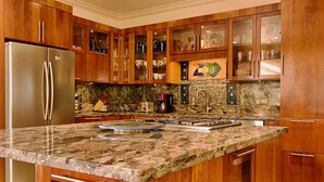 Una cocina con armarios de madera, encimera de granito y refrigerador de acero inoxidable.