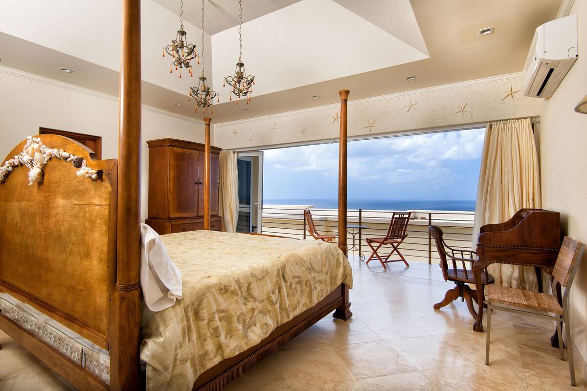 Une chambre à coucher avec un lit à baldaquin, des meubles en bois et une vue sur la mer.