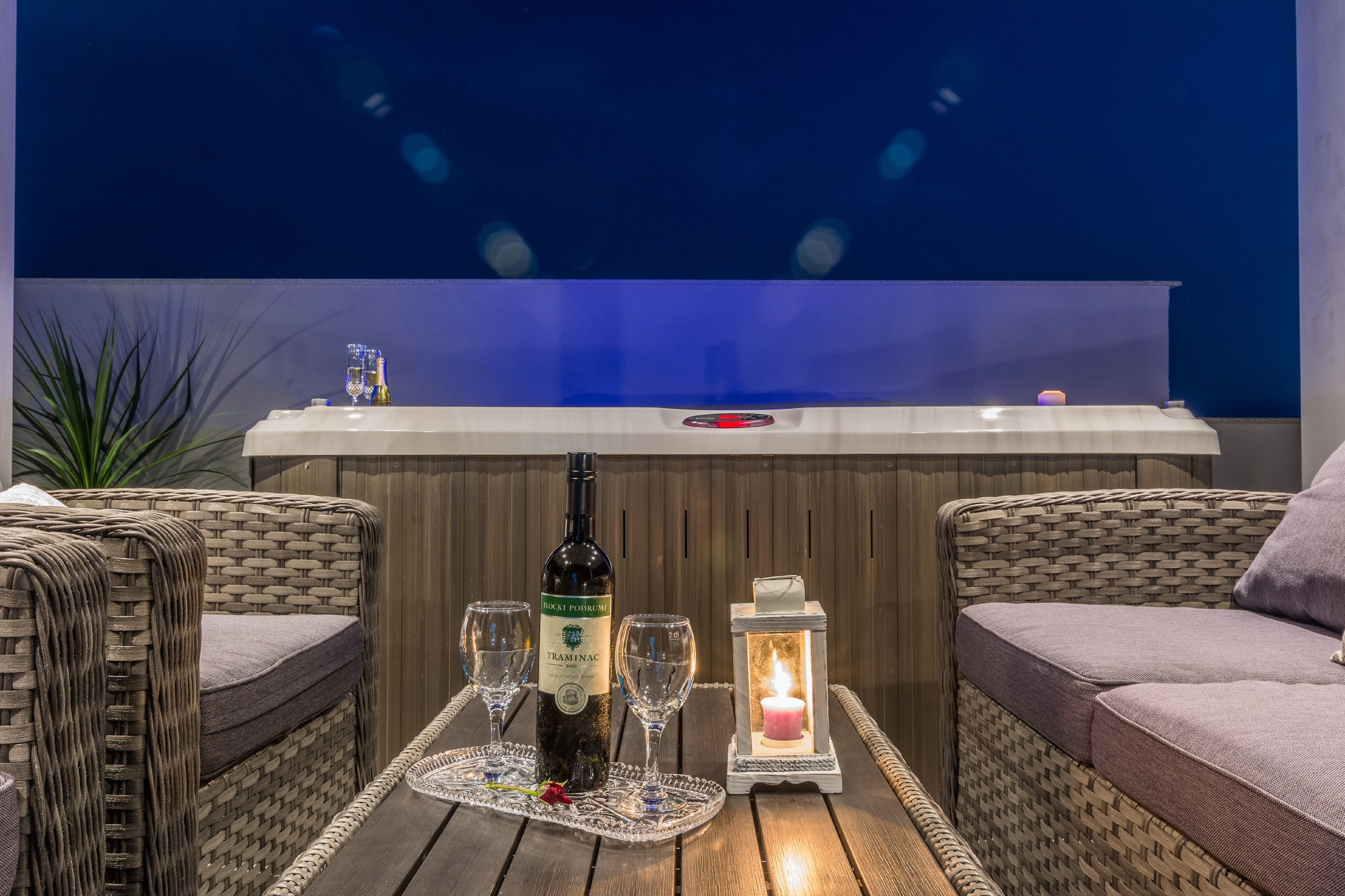 Un espace extérieur accueillant, aménagé avec des meubles en osier, une bouteille de vin, des verres et une bougie allumée sur une table en bois.