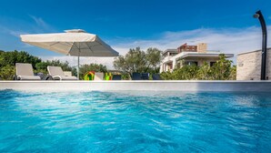 A swimming pool with lounge chairs and umbrellas, surrounded by modern buildings and greenery. - Sun Resort Nikolina (Bibinje)