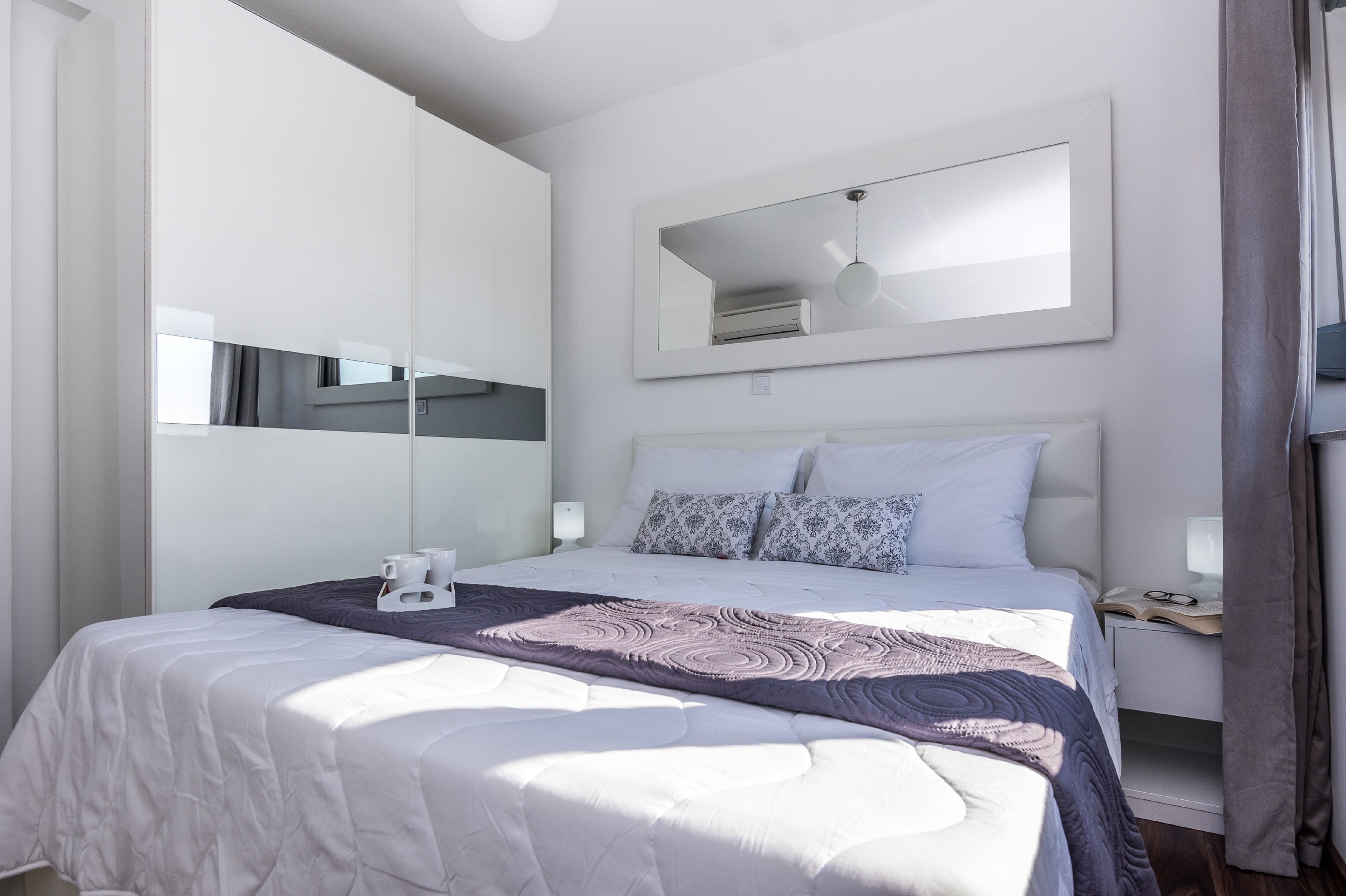 Un dormitorio moderno con una cama grande, una mesita de noche con lámpara, un espejo y un armario.