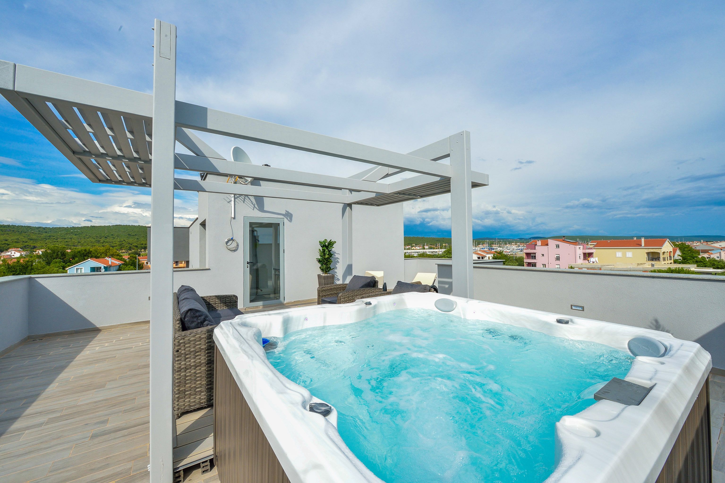 A rooftop hot tub with a pergola, wicker furniture, and a view of the surrounding neighborhood.