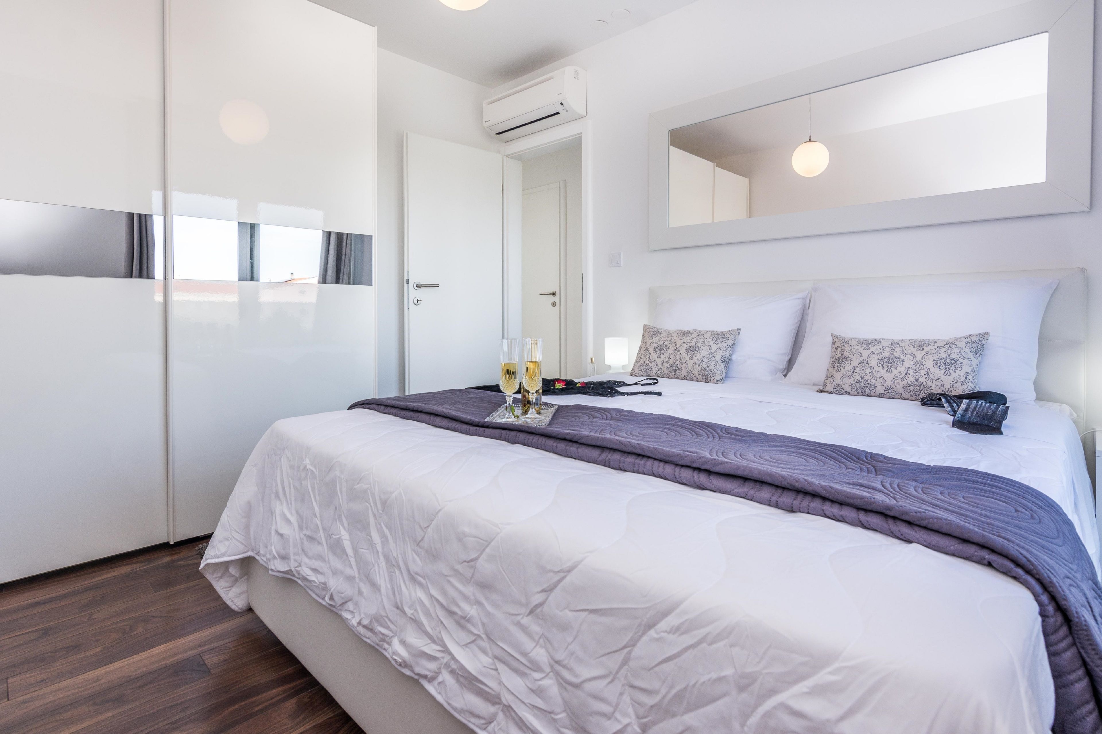Une chambre moderne avec un grand lit, des murs blancs, un miroir et une armoire.