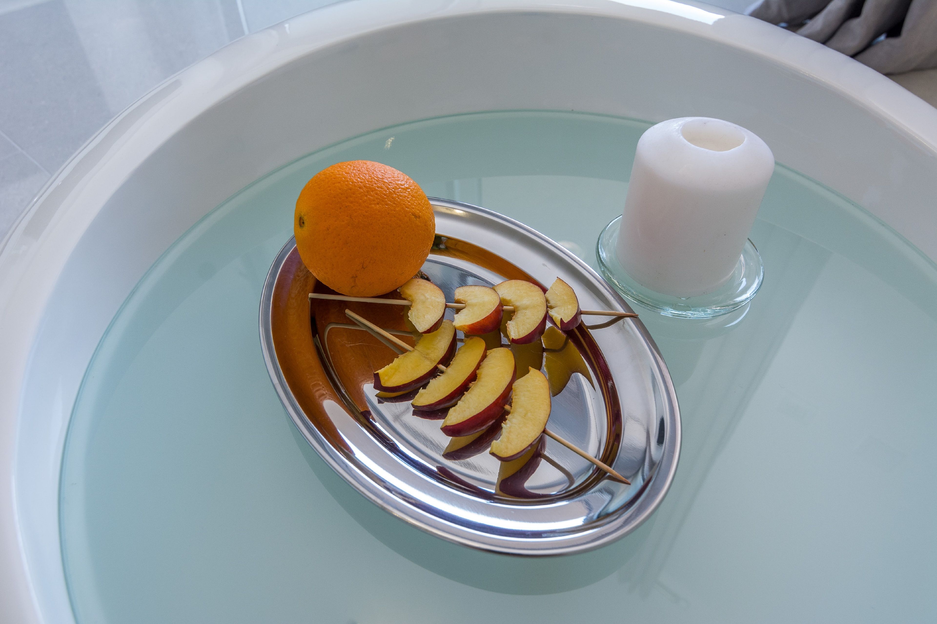A glass bowl containing apple slices and an orange on a tray.