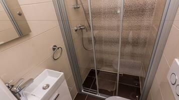 Un baño moderno con cabina de ducha de vidrio, un lavabo blanco y un inodoro.