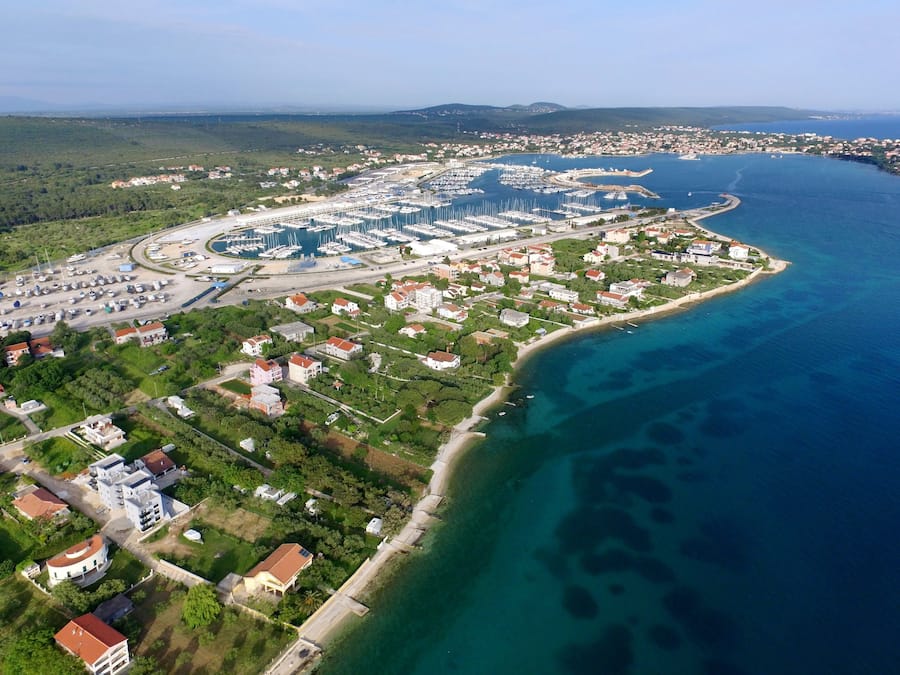 Vista aérea de un pueblo costero con un puerto deportivo, edificios residenciales y una playa.
