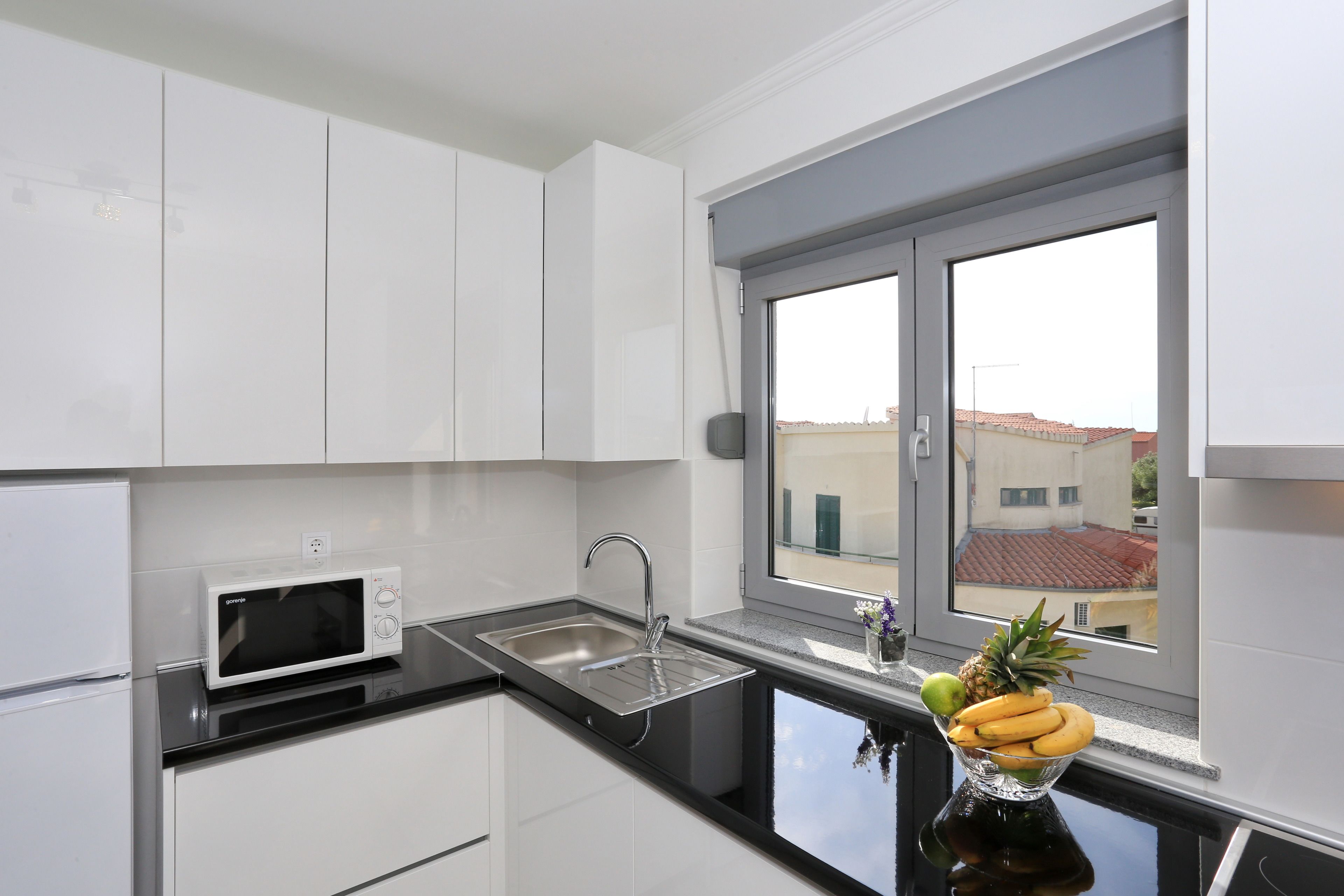 A modern kitchen with white cabinets, a black countertop, a stainless steel sink, and a window with a view of buildings.