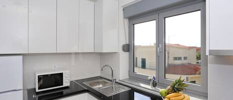 A modern kitchen with white cabinets, a black countertop, a stainless steel sink, and a window with a view of buildings.