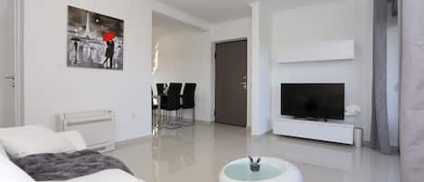 A modern living room with a white sofa, a flat-screen TV, a dining area with chairs, and a painting of the Eiffel Tower.
