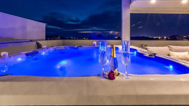 A hot tub with blue lighting, champagne glasses, and a rose on a rooftop terrace. - Sun Resort Nikolina (Bibinje)