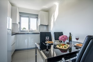 Cozinha moderna com armários brancos, uma mesa de jantar preta e uma janela que oferece luz natural.