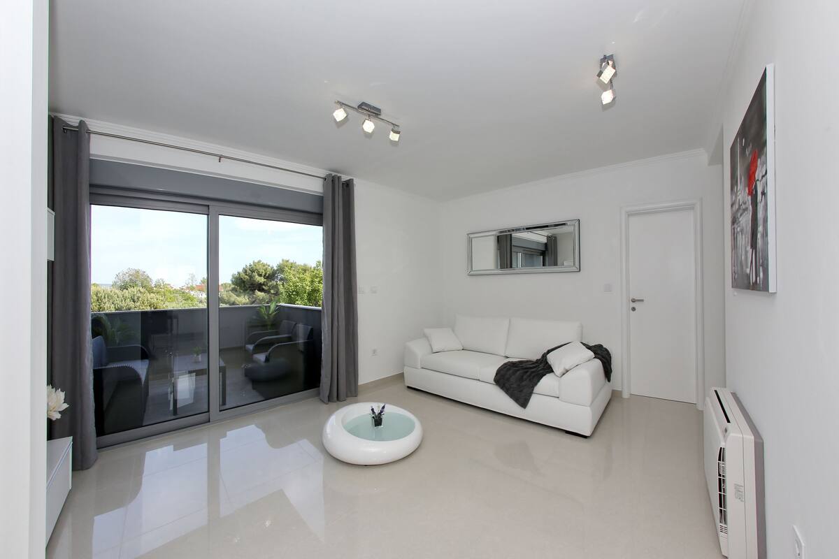 A modern living room with a white sofa, a glass coffee table, and a sliding glass door leading to a balcony.