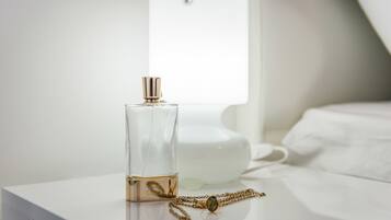 A clear glass perfume bottle with a gold cap and a gold chain necklace on a white bedside table.