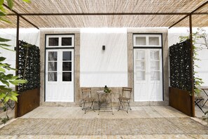 A covered patio area with two white doors, a small table with chairs, and a decorative plant. - bnapartments Carregal (Porto)