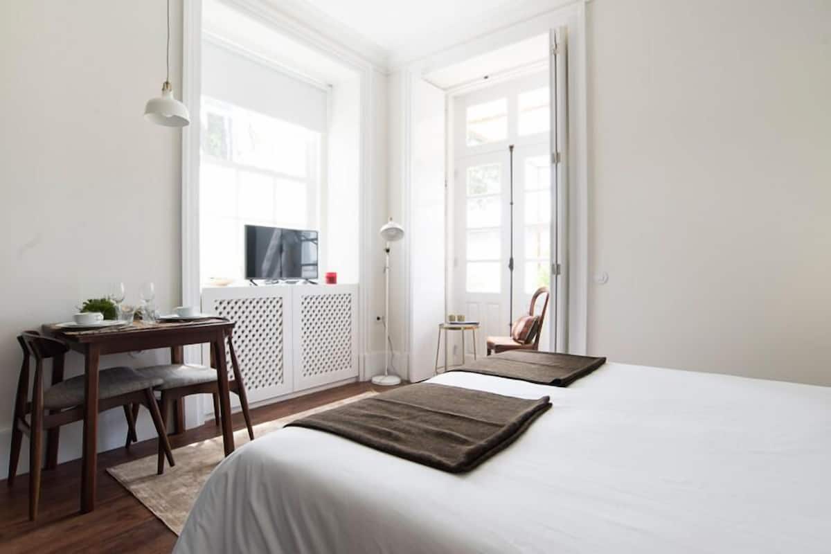 Un dormitorio con cama, escritorio y silla. Hay una ventana y una puerta.