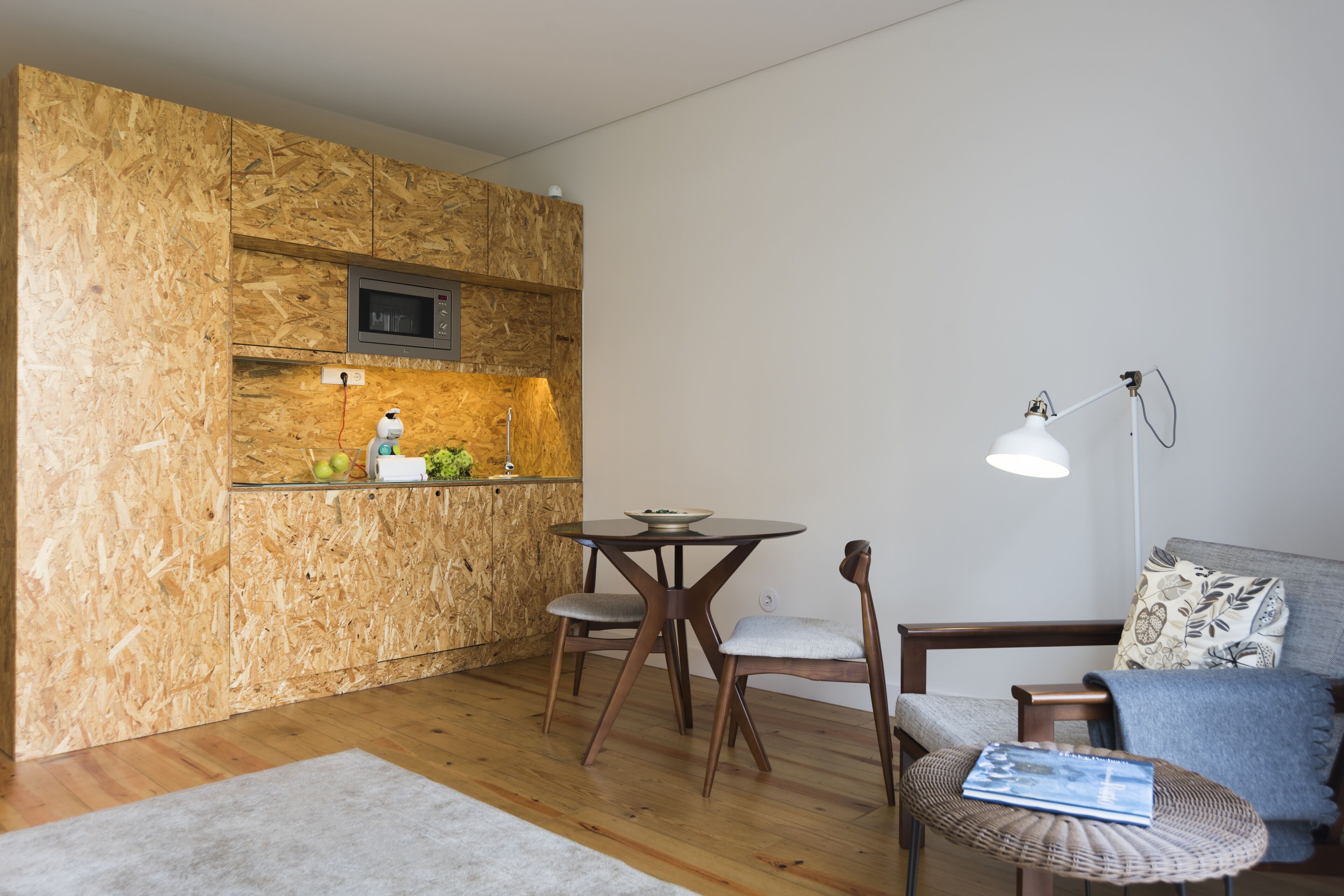 Um espaço de estar compacto com cozinha, incluindo micro-ondas e pia, uma mesa de jantar com duas cadeiras e um sofá com luminária.