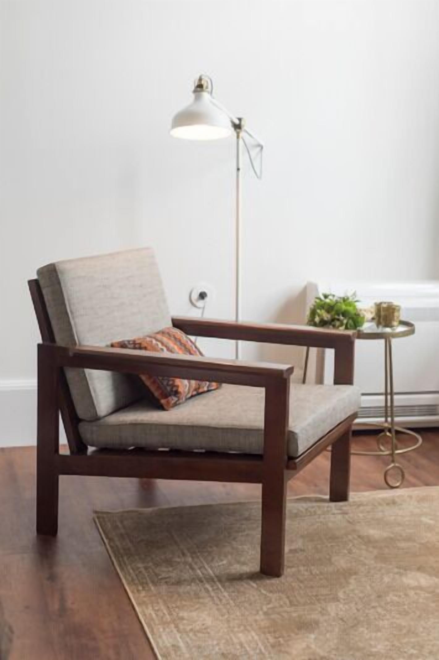 A chair with a cushion, a floor lamp, and a small table with a plant and a candle.