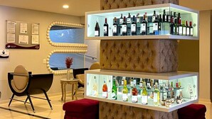 A modern lobby with a central display of wine bottles, a seating area with a red ottoman, and a wall-mounted information board.
