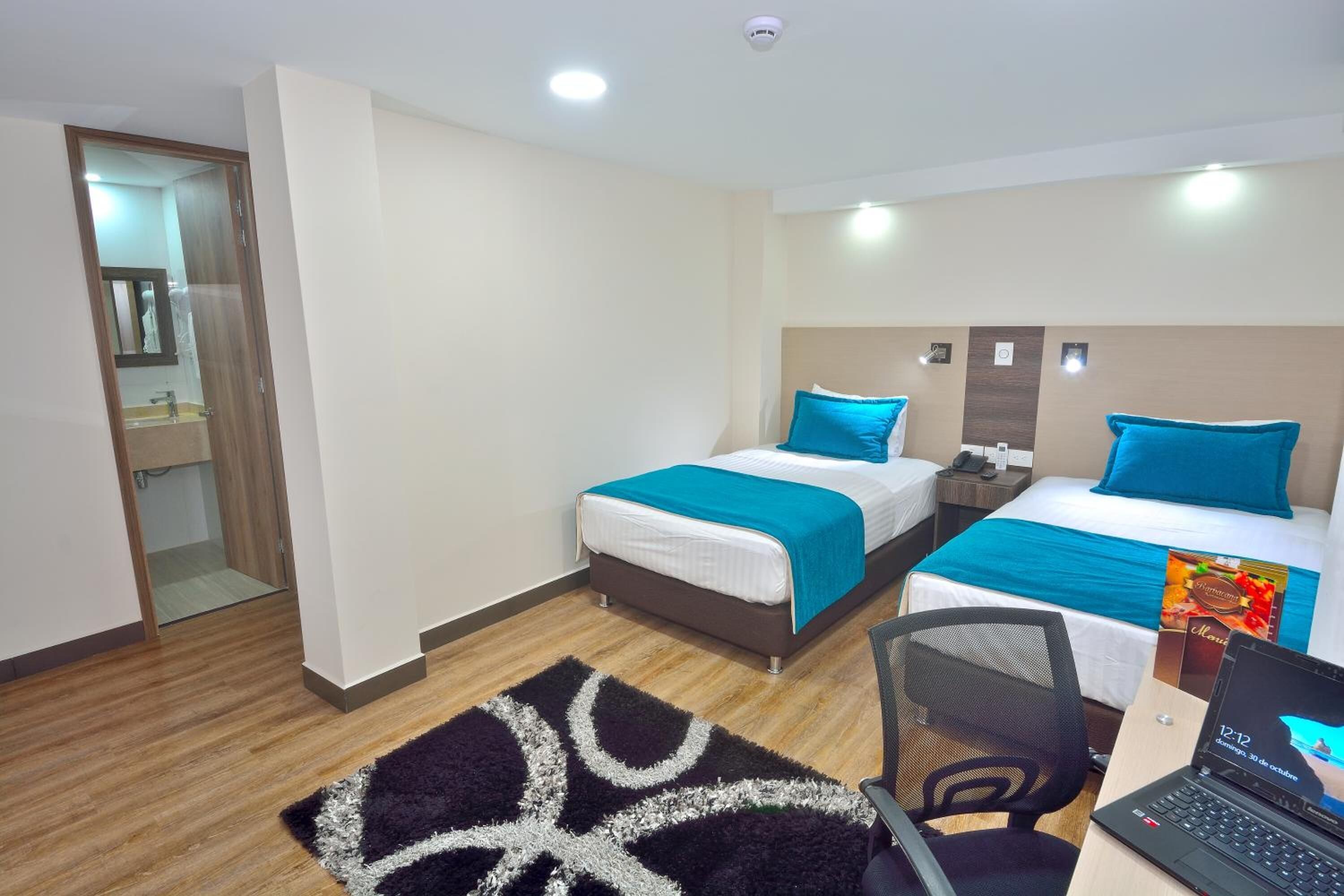 Habitación de hotel con dos camas, un escritorio con una computadora portátil, una silla y un tapete estampado.