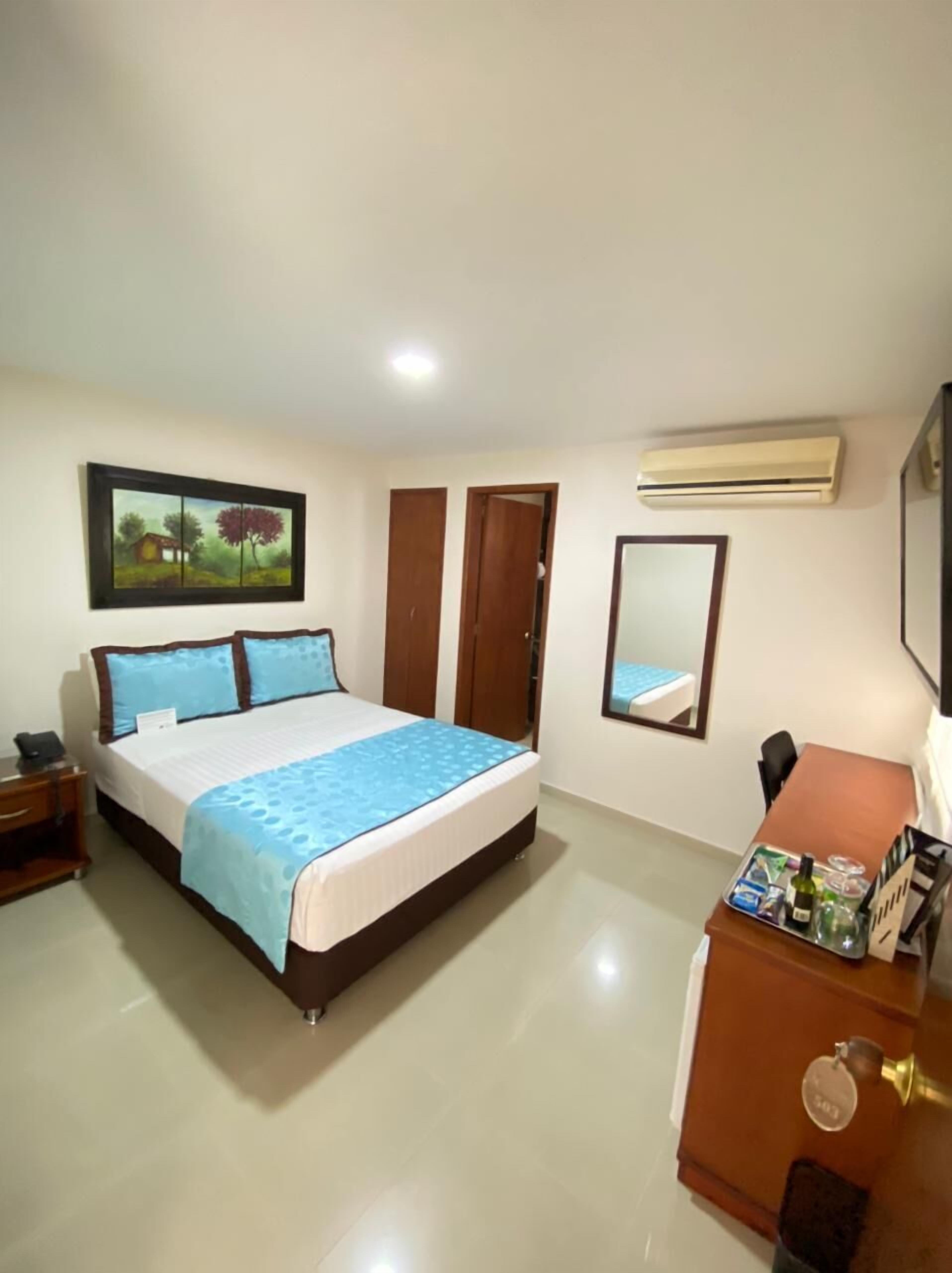 A hotel room with a bed, a desk, a dresser, an air conditioner, and a painting on the wall.