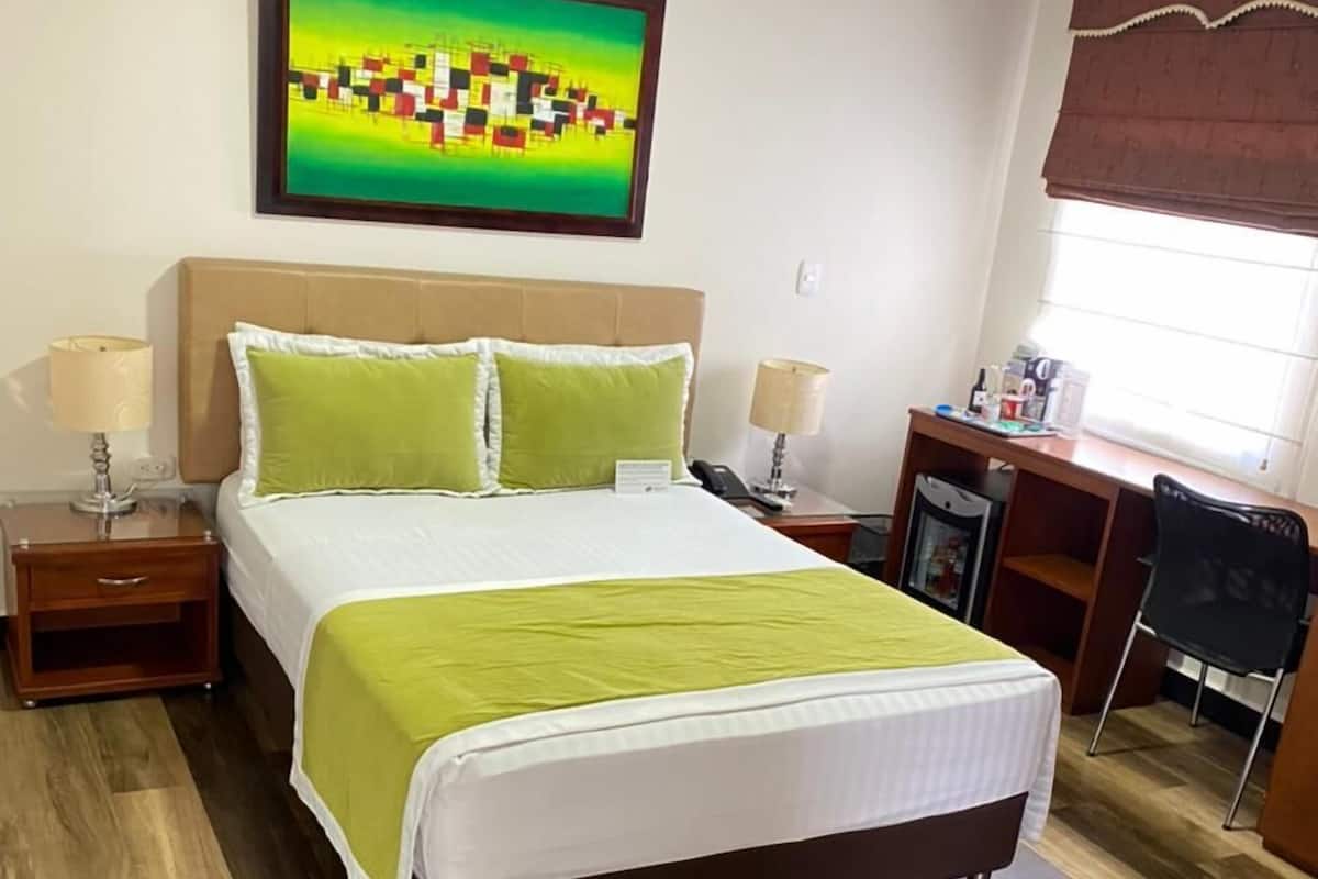 A hotel room with a large bed, two bedside tables, a desk, and a chair.