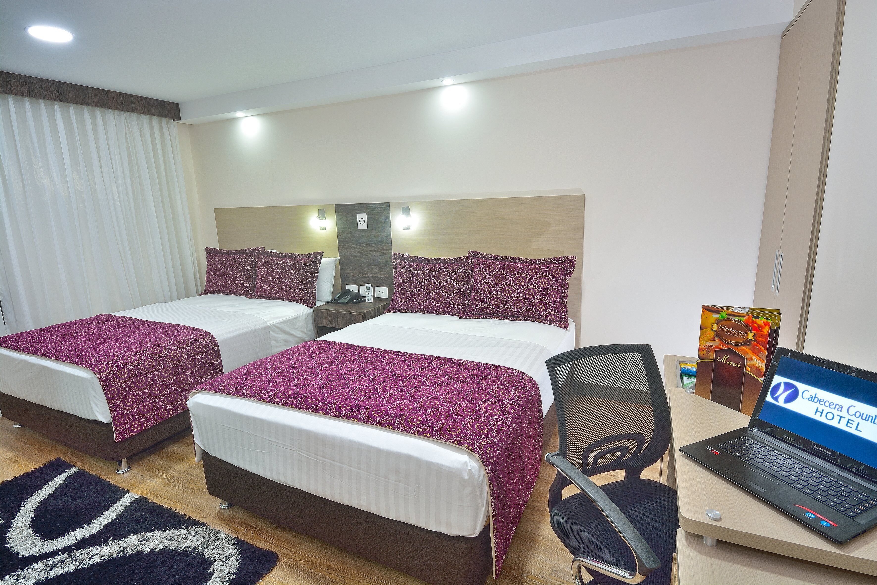 A hotel room with two beds, a desk with a laptop, and a chair.
