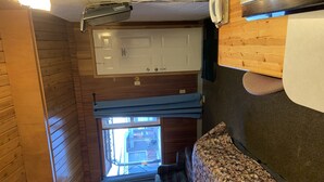 Una habitación compacta con interior de madera, una ventana con persianas, un sofá y una pequeña mesa.