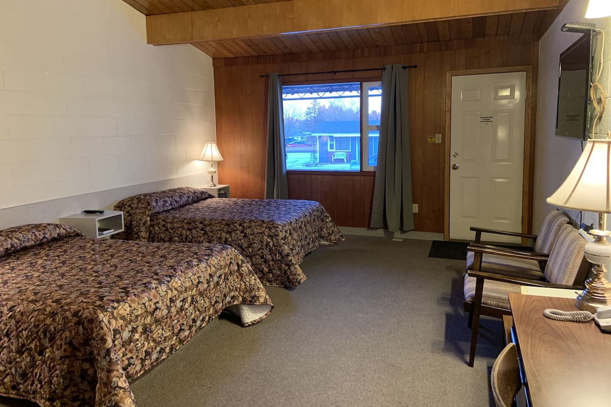 A room with two beds, a desk, a chair, a lamp, and a window with curtains.