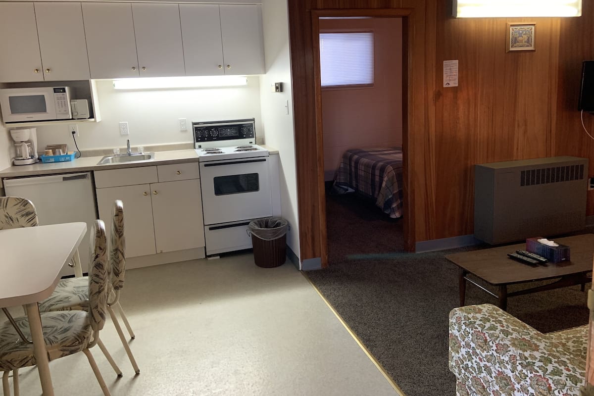 A compact kitchen with a microwave, stove, and sink. There's a small trash bin and a dining area with a table and chairs.