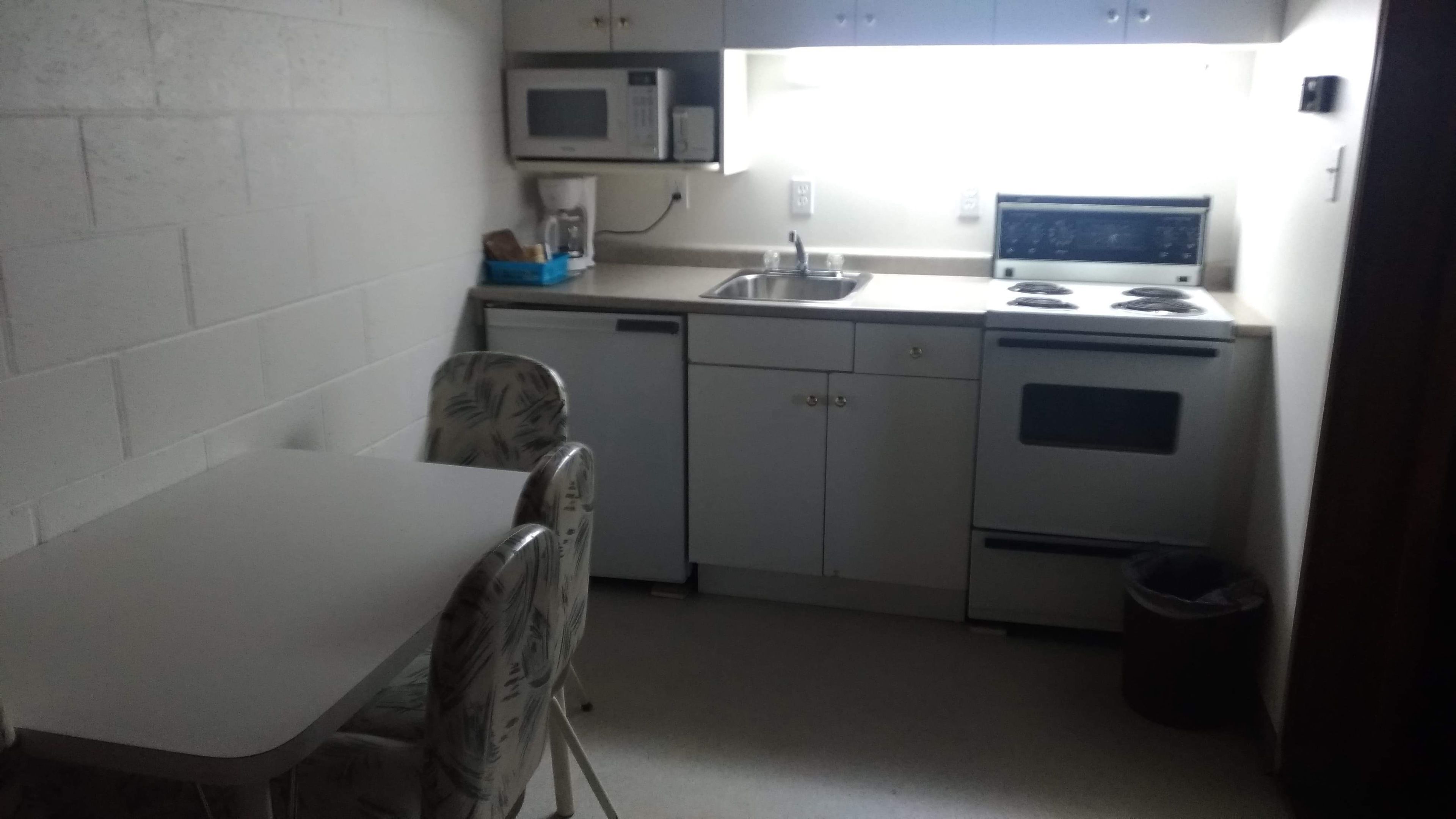 A compact kitchen with a white countertop, a microwave, a coffee maker, a sink, and a stove.