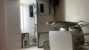 Una cocina compacta con armarios blancos, microondas, refrigerador pequeño y cafetera.